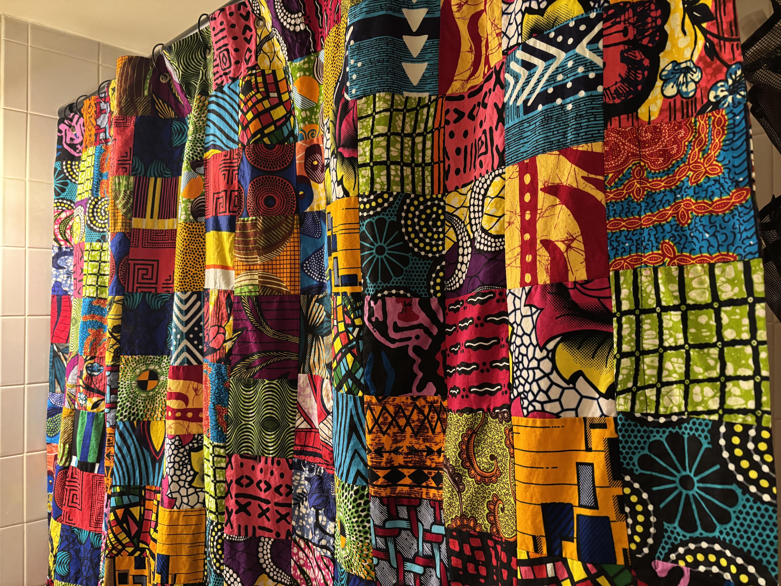 a portion of my african wax print shower curtain hanging in front of my bathtub. it's made up of several fabric remnants that are sewn together, so it looks rather quilt-like. the colors are extremely vibrant and vary between different multicolored shades and various patterns of lines, flowers, dots and waves. 

there's a shower liner behind it, which is hidden by the curtain.